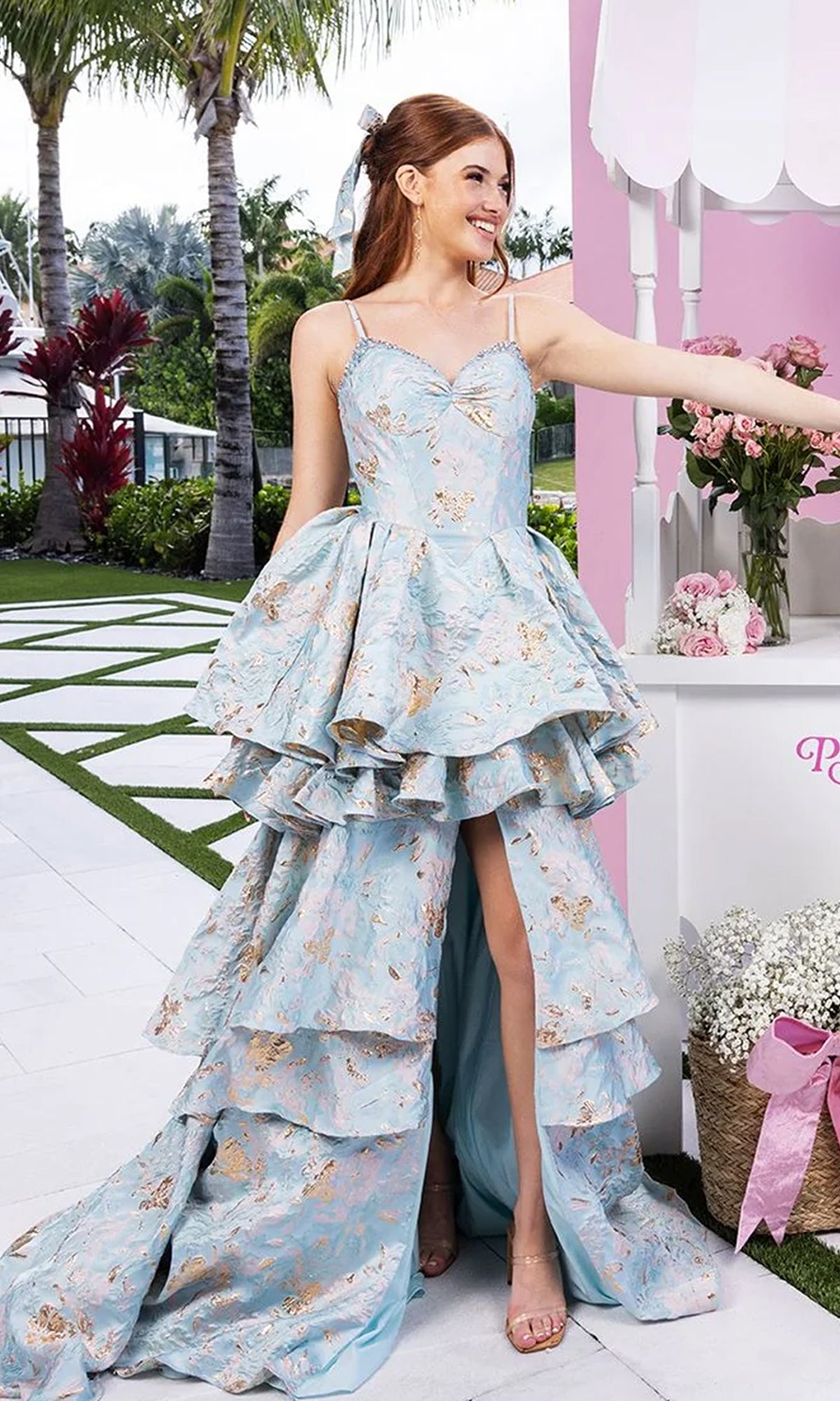 A woman in the blue Long Formal Dress: Portia and Scarlett XO181 with a tiered skirt smiles outdoors near a pink and white flower-adorned cart.